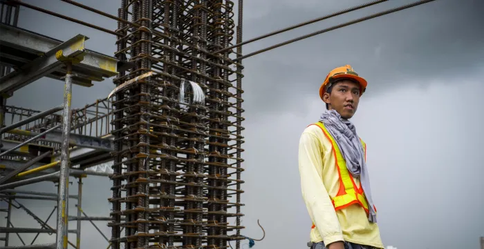 a young male construction worker in a high-rise building behind dark, cloudy skies
